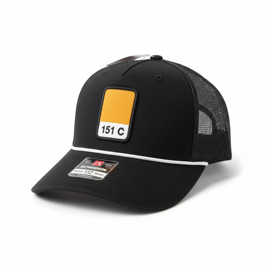 BOX SEAT black trucker hat featuring a Pantone 151C orange square patch and a white decorative cord on the brim.